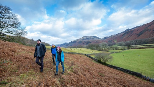 Three friends walking along a path at Bird How with sheep and the surrounding fells in the background